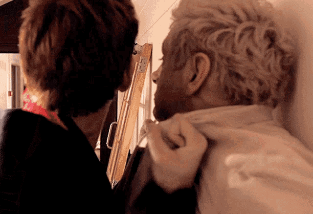 two men are standing next to each other and one of them is adjusting the other 's shirt .