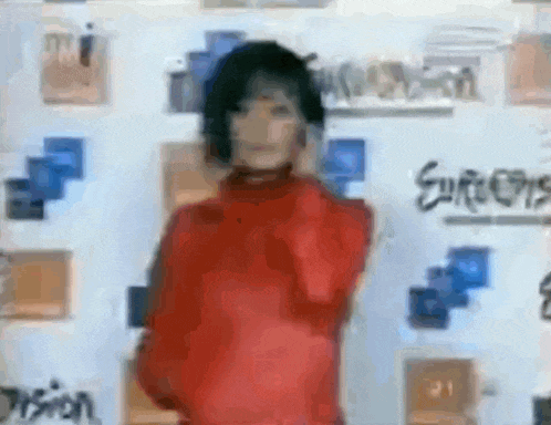 a woman in a red sweater is dancing in front of a wall with graffiti on it .