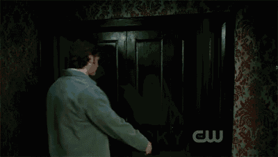 a man in a green jacket is standing in front of a door with the words `` spooky cw '' written on it .