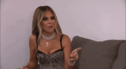 a woman is sitting on a couch wearing a cross necklace and a leopard print top .