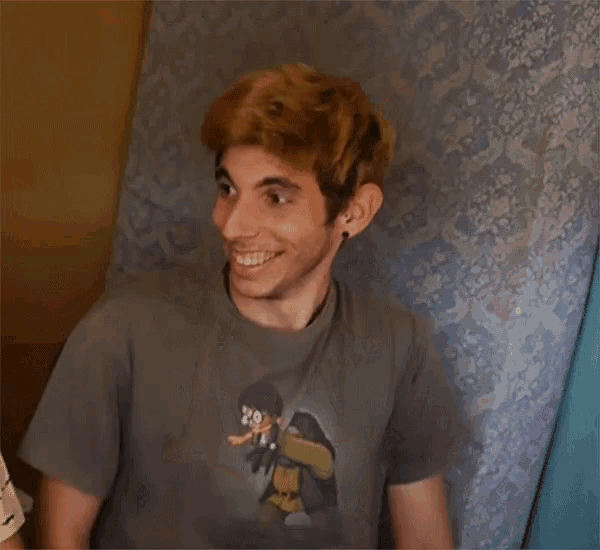 a young man wearing a grey shirt with a cartoon character on it smiles