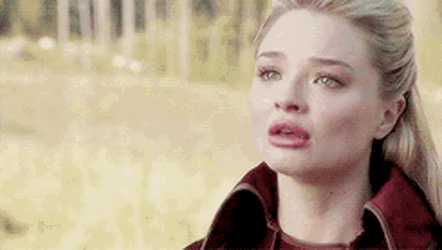 a woman is standing in a field with her mouth open and a red jacket on .