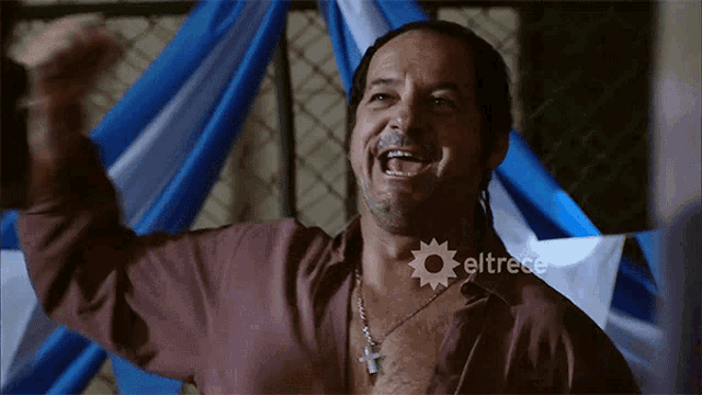 a man with a cross around his neck is screaming in front of a banner that says eltrece