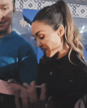 a woman in a ponytail is talking to a man in a blue shirt while looking at her phone .