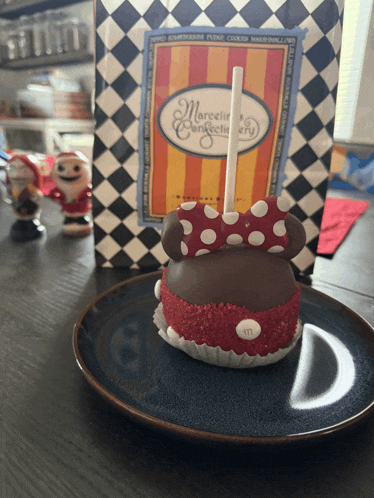 a blue plate with a mickey mouse cake on it in front of a bag that says marcel 's confectionery