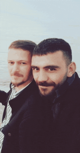 two men posing for a picture with one wearing a black jacket