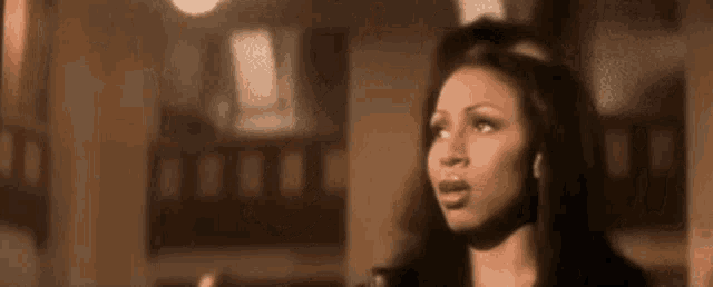 a woman is singing into a microphone in a room and looking at the camera .