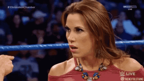 a woman is standing in a wrestling ring wearing a red top and necklace .