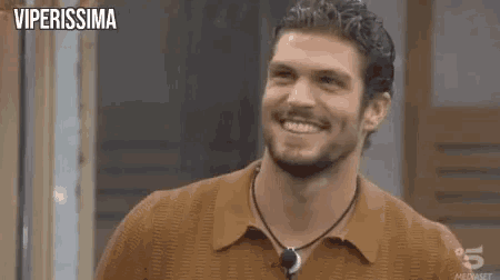 a man with a beard is smiling while wearing a brown shirt and a necklace .