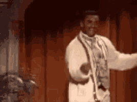 a man in a white suit is dancing on a stage in front of a red curtain .