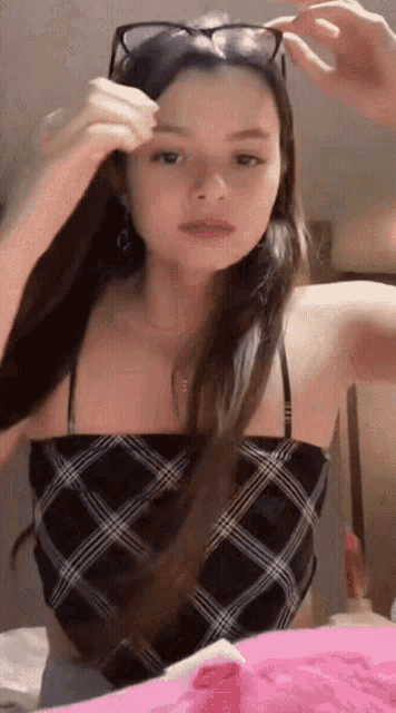 a woman wearing sunglasses and a plaid top is adjusting her hair .