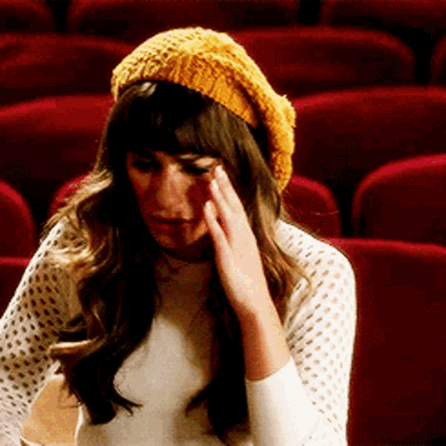 a woman wearing a yellow hat is sitting in a row of red seats