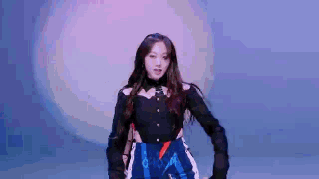 a woman in a black shirt and blue shorts is dancing in front of a blue and purple background .