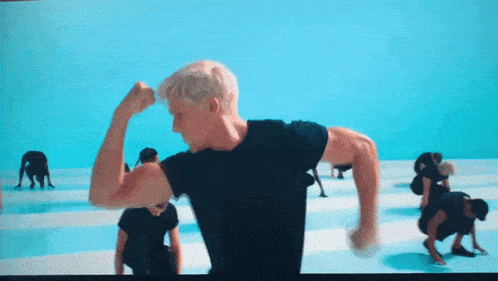 a man in a black shirt flexes his muscles in front of a group of people