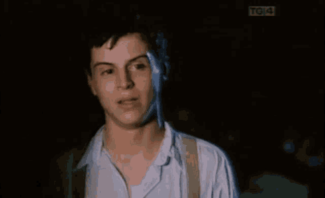 a man in a white shirt and suspenders is standing in the dark with a tg4 sign in the background