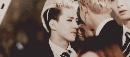 a man in a suit and tie is touching another man 's nose while standing next to each other .