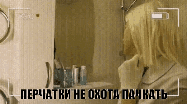 a woman wearing gloves is looking at herself in a bathroom mirror while being recorded