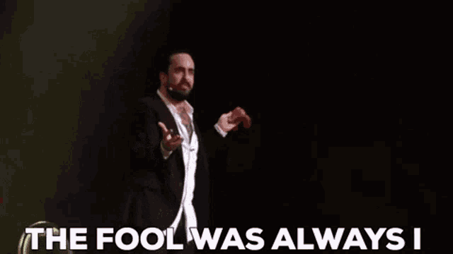 a man in a suit and white shirt is holding a red object and says the fool was always i