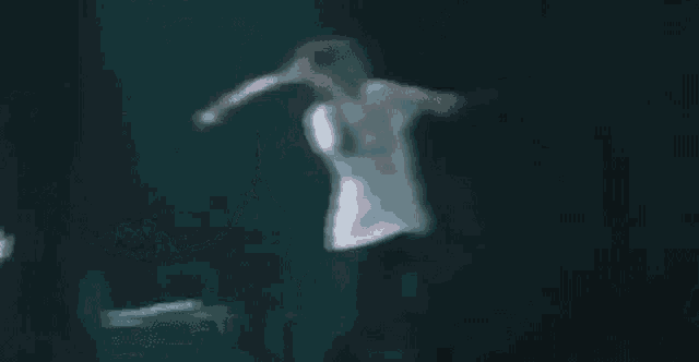 a woman in a white shirt is dancing in a dark room with water coming out of her mouth .