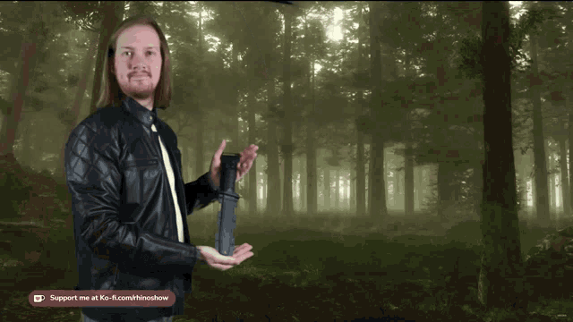a man in a leather jacket holds a camera in front of a forest