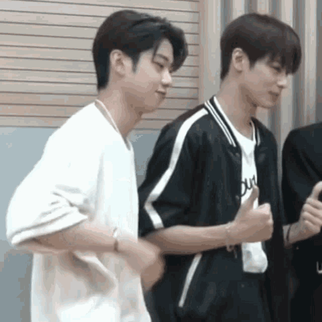 two young men are standing next to each other and giving each other a thumbs up .