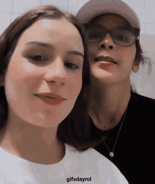 a woman wearing glasses and a hat is standing next to another woman .