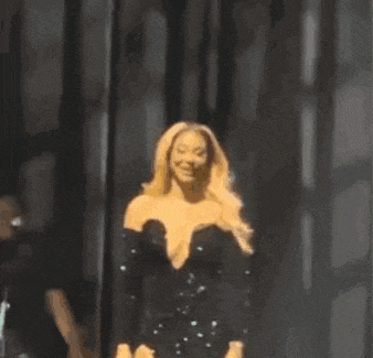 a woman in a black dress is standing on a stage and smiling at the camera .