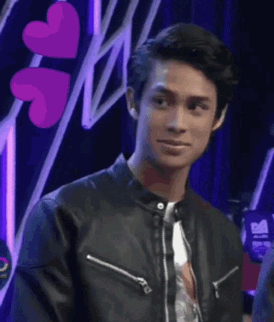 a young man wearing a black leather jacket is standing in front of a purple heart .