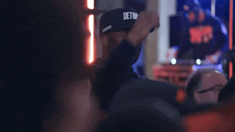a man wearing a detroit hat is dancing in a dark room .