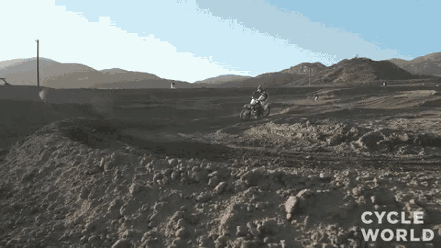 a person riding a dirt bike on a dirt road with the words cycle world written on the bottom