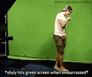 a man is standing in front of a green screen with the caption " * shyly hits green screen when embarrassed * "