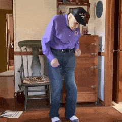 a man in a purple shirt and black hat is dancing in a living room