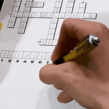 a person 's hand is holding a pen over a crossword puzzle on a piece of paper