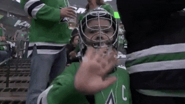 a young boy wearing a hockey helmet is giving a high five while sitting in the stands at a hockey game .