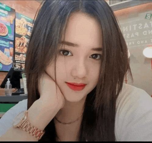 a woman wearing a watch and red lipstick takes a selfie in front of a pizza menu