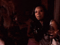 a woman is holding a glass of wine while sitting in a dark room .