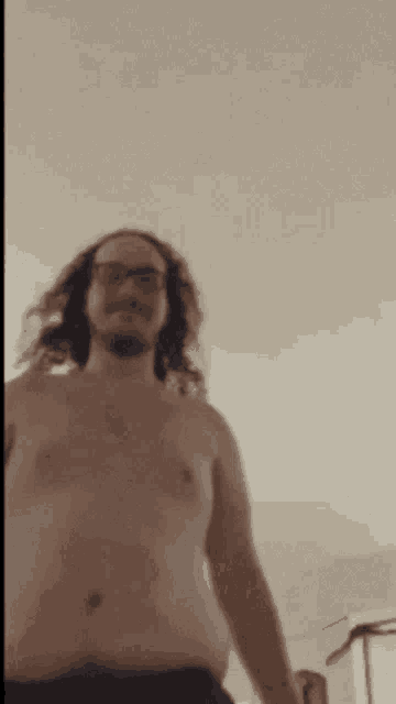 a shirtless man with long hair and glasses is standing in front of a white wall