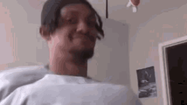 a man wearing a hat and a white shirt is making a funny face in a bedroom .