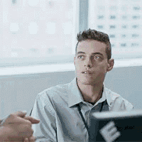 a man is sitting at a table in front of a laptop computer and looking at something .