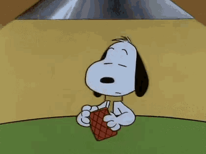 snoopy is sitting at a table with four playing cards and pointing at them .