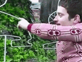 a man in a pink sweater is standing in front of a fence and holding a rope .