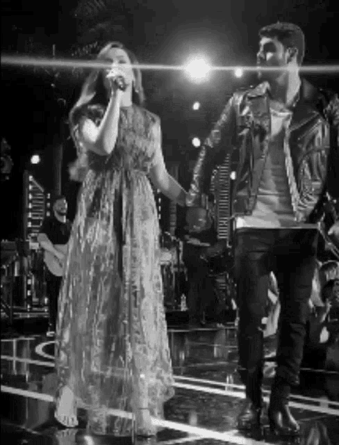 a woman singing into a microphone while a man stands behind her