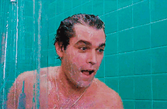 a man is screaming in a shower with a blue tile wall behind him