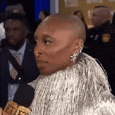 a woman with a shaved head and earrings is wearing a fur coat and holding a microphone .