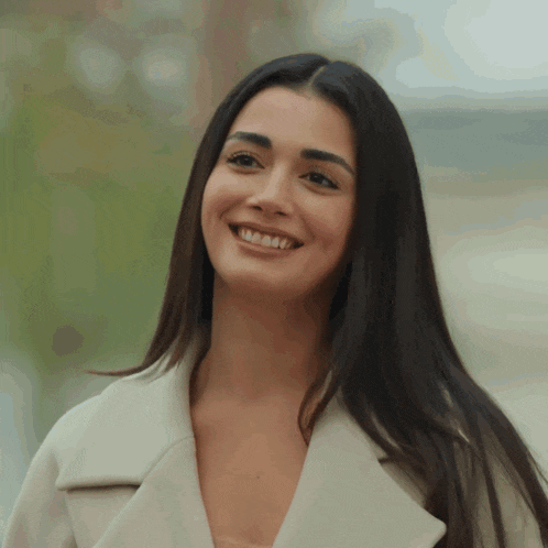 a woman with long dark hair is smiling and wearing a white jacket