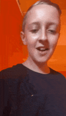 a young boy in a black shirt is making a funny face in front of an orange wall .