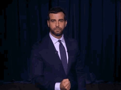 a man in a suit and tie is standing in front of a curtain
