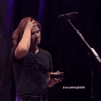 a man in a black shirt is standing in front of a microphone on a stage holding something in his hand .