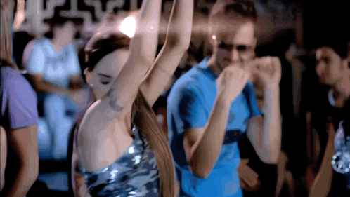 a woman in a silver dress is dancing in front of a man in a blue shirt