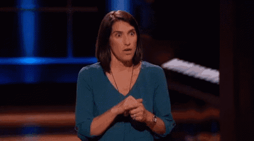 a woman in a blue shirt is standing on a stage with her hands folded and a surprised look on her face .